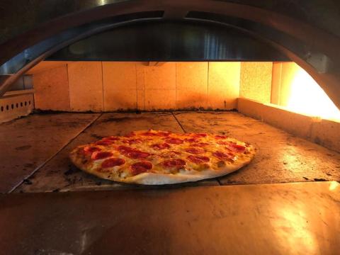 This image shows a pepperoni pizza baking inside a wood-fired pizza oven