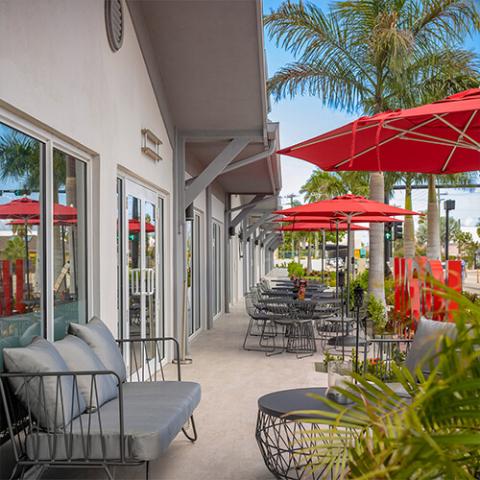 The image shows an outdoor seating area of a modern cafe or restaurant, featuring stylish, black wire-frame chairs and round tables