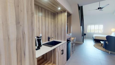 The image shows a modern, well-lit room that appears to be a combination of a small kitchenette and a bedroom
