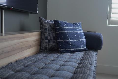 The image shows a stylish interior setting, featuring a part of a room with a plush daybed covered in textured fabric, adorned with two decorative pillows