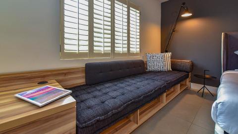 This image depicts a modern bedroom interior featuring a window with white shutters, allowing soft light to filter through