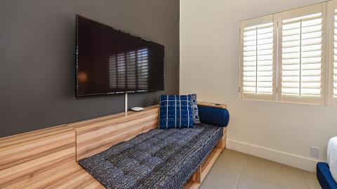 This image shows a modern room interior featuring a wooden daybed covered with a patterned blue blanket and matching cushions