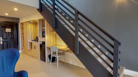 The image shows a modern interior setting of a room that features a set of wooden stairs with a dark metal railing, leading upwards