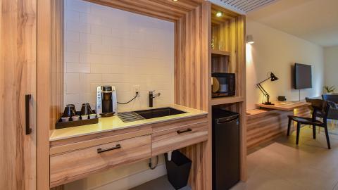 This image showcases a modern, compact kitchenette and an adjoining small office space, all unified by a cohesive and warm wood design
