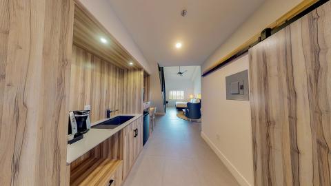 This image shows a modern interior setting composed of a small kitchenette area leading into a bedroom