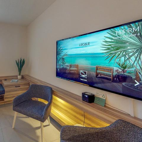 This image shows a modern, well-decorated room featuring a large, wall-mounted television displaying a tranquil beach scene