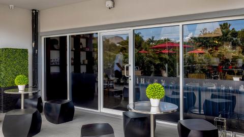The image shows a modern outdoor seating area adjacent to a building with large sliding glass doors