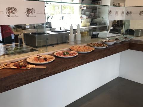 This image depicts the interior of an urban Italian kitchen, specifically a counter serving area with a variety of Italian dishes on display
