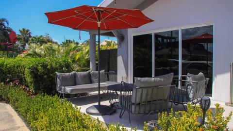 This image features an outdoor patio area adorned with a large red umbrella providing shade over a variety of stylish outdoor furniture