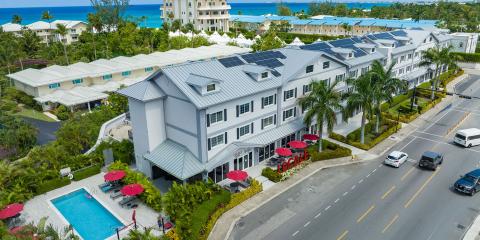 This image shows an aerial view of a modern, multi-storied building with gray walls and a metal roof, part of which is outfitted with solar panels