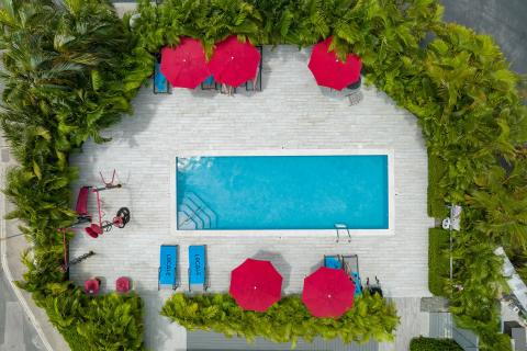 This image features an aerial view of a pool area surrounded by a paved terrace with neatly arranged amenities
