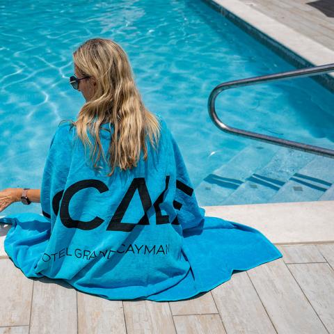 The image features a woman sitting by a pool, her back to the camera