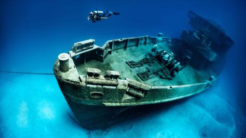 This image features an underwater scene with a large sunken shipwreck at the bottom of the ocean