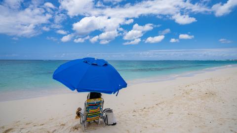 This image shows a beautiful beach scene with a bright blue beach umbrella sheltering a beach chair