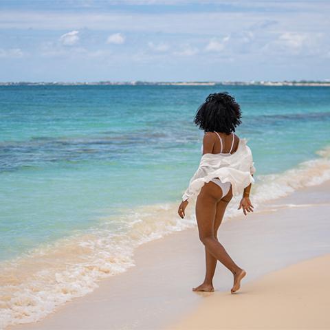 The image shows a woman standing on a beautiful sandy beach, facing the ocean