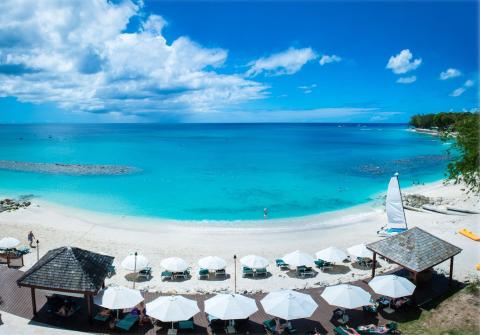 This is an image of a picturesque beach with a clear, blue ocean and a vibrant blue sky speckled with clouds