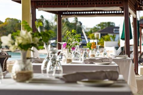 The image shows an elegantly set outdoor dining area at a beachside restaurant