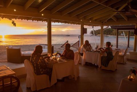 This image shows a beautiful dining scene at a beachside restaurant during sunset
