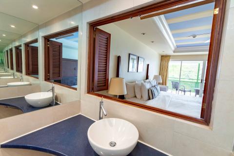 This image shows a stylish bathroom with a large mirror reflecting an image of an adjacent bedroom