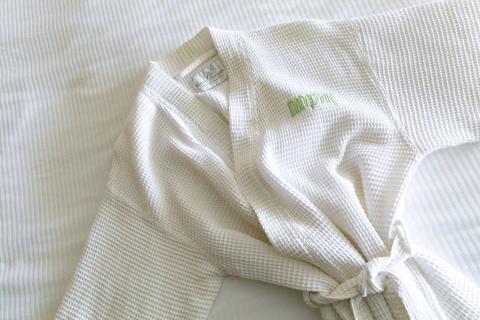 The image shows a white waffle-weave bathrobe, laid out on a textured white bedspread