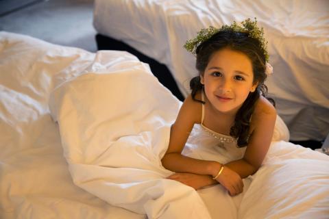 The image shows a young girl lying on a bed with white sheets