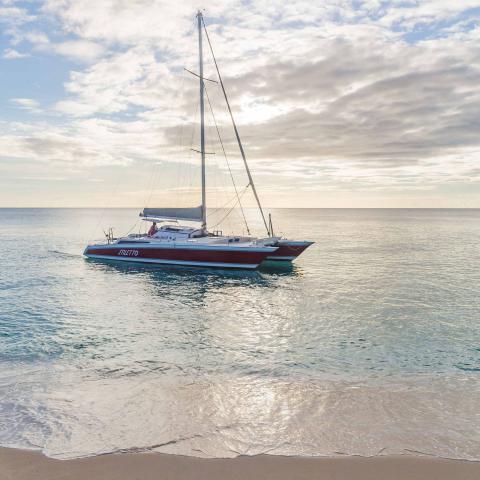 The image shows a large sailboat moored near a beach