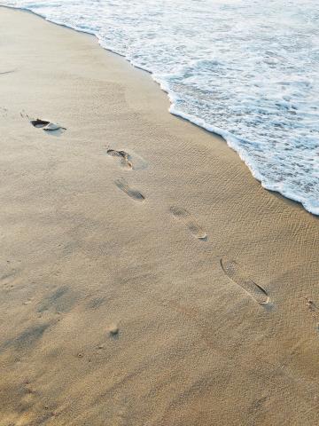The image captures a sandy beach with a series of footprints leading away from the viewer towards the upper left corner