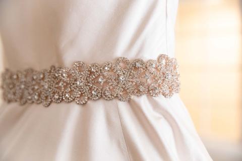 This image features a close-up view of a decorative belt on a white dress, possibly a wedding gown