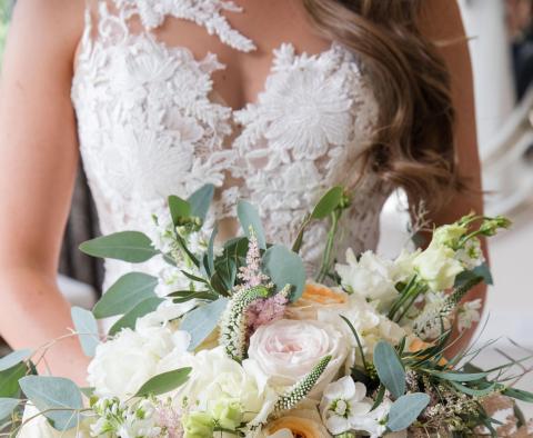 This image features a close-up view of a woman in a detailed lace wedding dress, holding a beautiful bouquet of flowers