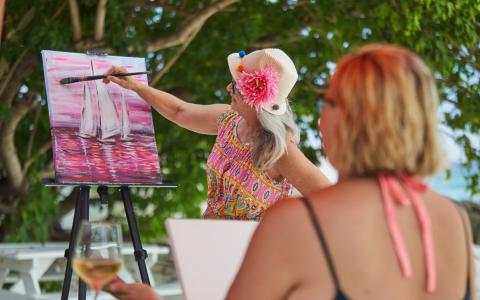 This image shows two women engaged in an outdoor painting activity, likely an art class