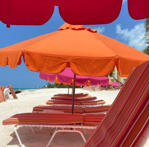 This image captures a vibrant and inviting beach scene featuring multiple brightly colored beach umbrellas in shades of orange and pink