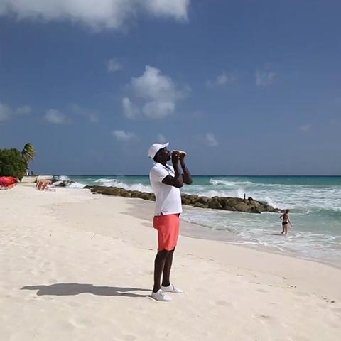 The image features a person standing on a sandy beach under a clear blue sky