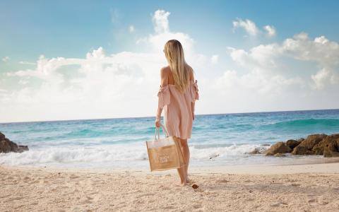 This image captures a woman standing on a sandy beach, facing the turquoise ocean