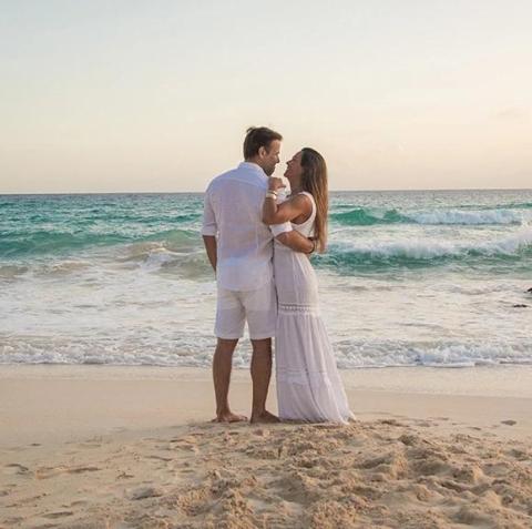 The image depicts a couple standing on a beach at sunset