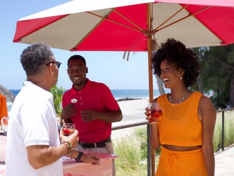 This image captures a lively scene at a beach where three people are engaging in conversation under a bright red umbrella