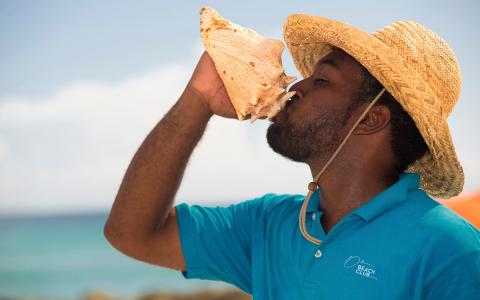 The image shows a man wearing a straw hat and a light blue polo shirt labeled "Beach Club Spa