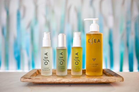 The image displays four different cosmetic products arranged on a wooden tray, with a decoratively blurred blue and white background