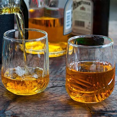 The image shows two glasses of amber-colored liquid, which appears to be whiskey