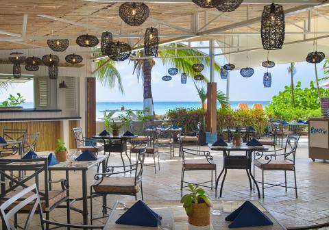 The image shows a beautiful seaside restaurant with an open design that allows for a scenic view of the beach and ocean