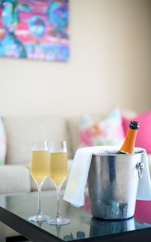 This image features a cozy indoor setting with two champagne flutes filled with a bubbly beverage, displayed prominently on a glass table
