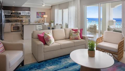 The image shows a modern and stylishly decorated living room with an open-plan layout that includes a kitchen area