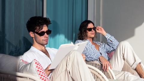 The image shows two people sitting comfortably in wicker chairs, bathed in sunlight, possibly on a balcony or an outdoor patio area