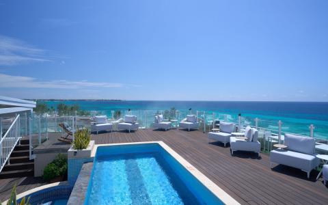 The image shows a stylish outdoor lounge area that overlooks a stunning turquoise ocean