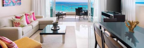 This image shows a luxurious modern living room with a stunning beachfront view
