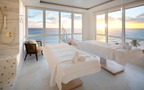 The image shows a luxurious spa or relaxation room with two massage tables covered in white linens