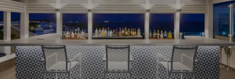 The image shows an elegant outdoor bar area set against a night-time backdrop