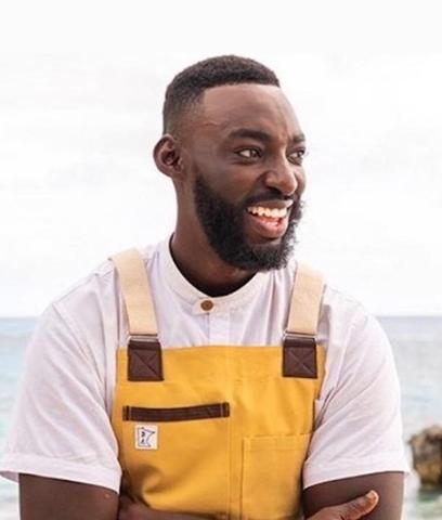 The image features a man smiling broadly, dressed in a yellow and white outfit that includes yellow overalls with leather-like straps and a white top