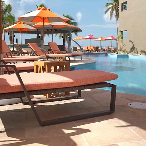 The image shows a sunny poolside scene with several sun loungers featuring cushions orange in color