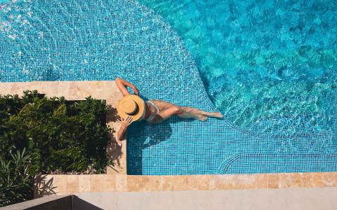 This image features an individual lounging at the edge of a beautiful, sparkling turquoise swimming pool