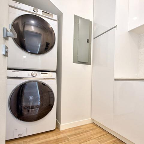 This image shows a modern, compact laundry room featuring a stacked washer and dryer setup from Samsung